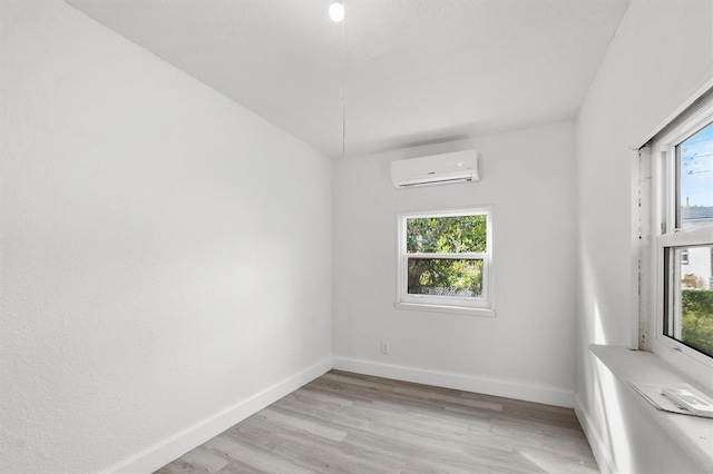 empty room featuring light hardwood / wood-style flooring, a wall mounted AC, and plenty of natural light