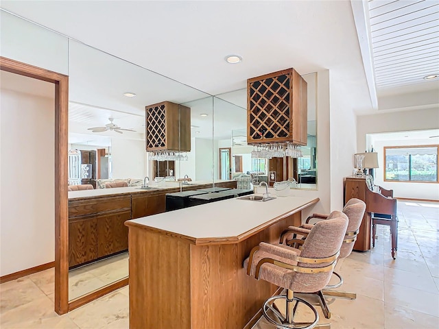 kitchen with kitchen peninsula, a kitchen bar, ceiling fan, sink, and light tile patterned floors