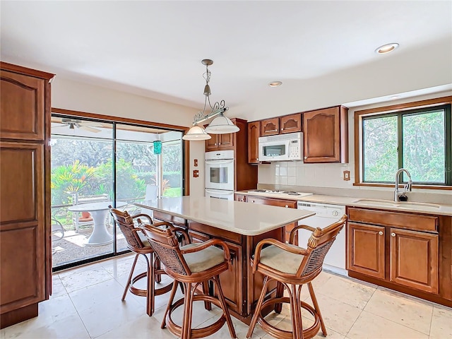 kitchen with sink, hanging light fixtures, backsplash, white appliances, and a kitchen island