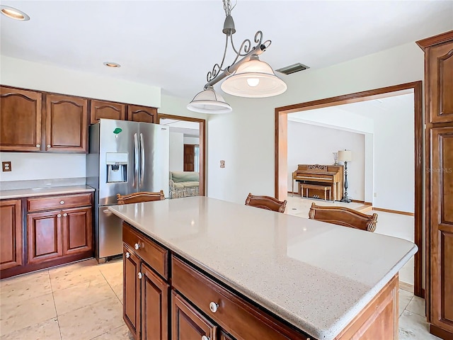 kitchen featuring light stone counters, a center island, hanging light fixtures, and stainless steel refrigerator with ice dispenser