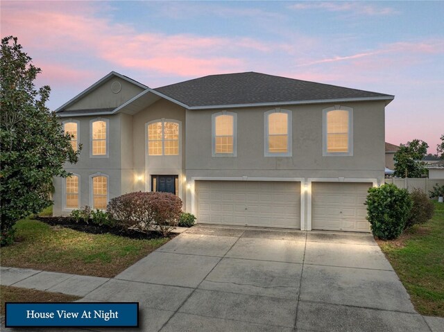 traditional-style home featuring roof with shingles, stucco siding, an attached garage, and concrete driveway