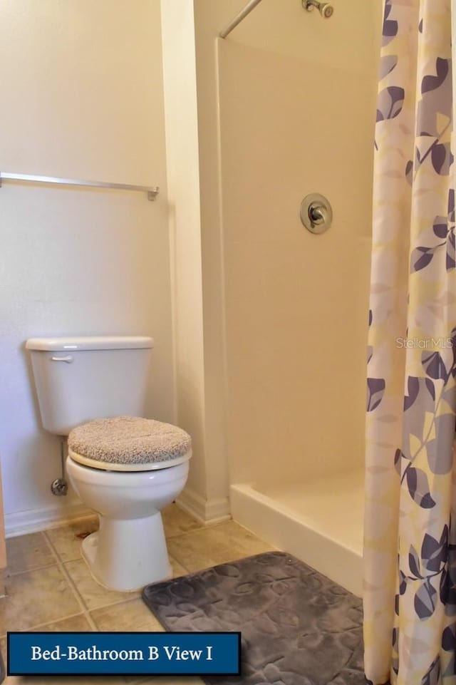 bathroom with a stall shower, baseboards, toilet, and tile patterned flooring