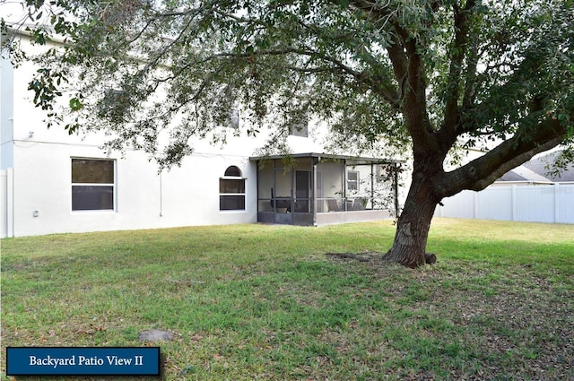 rear view of property with stucco siding, a sunroom, fence, and a yard