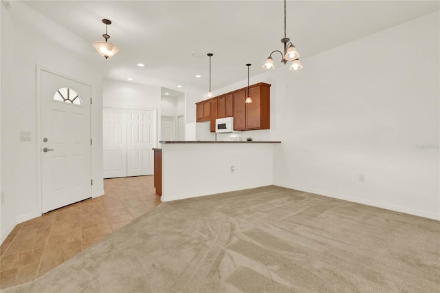 kitchen with dark stone counters, light colored carpet, pendant lighting, and kitchen peninsula