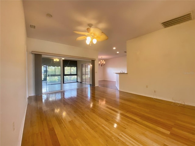 empty room with hardwood / wood-style floors and ceiling fan with notable chandelier