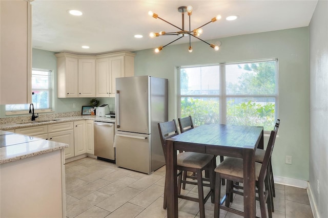 kitchen featuring sink, appliances with stainless steel finishes, light stone counters, white cabinetry, and a chandelier