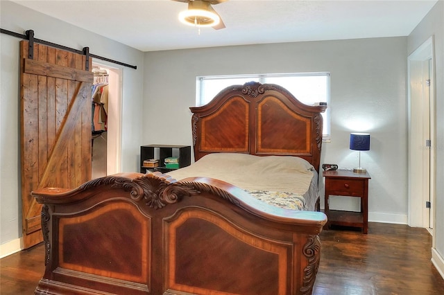 bedroom with dark wood-style floors, a barn door, and baseboards