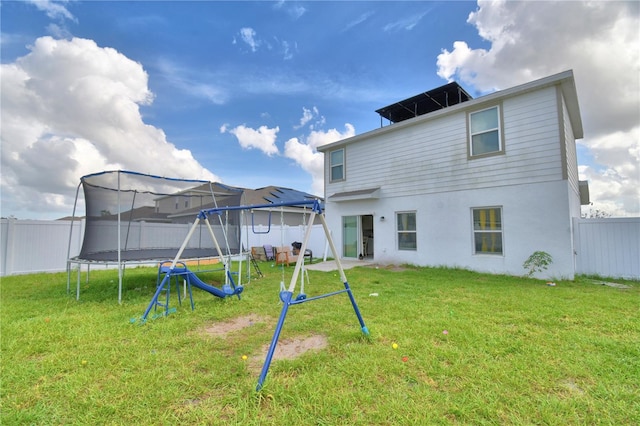 back of house featuring a trampoline and a lawn