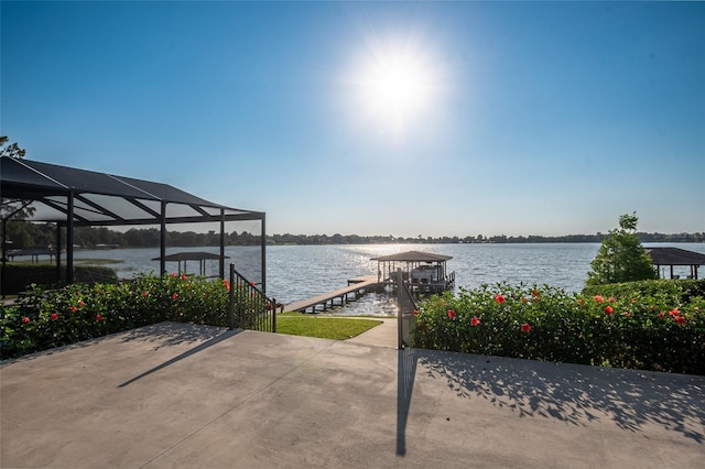 view of patio with a water view, a dock, and glass enclosure