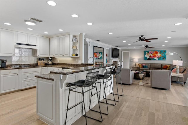 kitchen featuring a kitchen breakfast bar, light hardwood / wood-style flooring, white cabinetry, and dark stone countertops