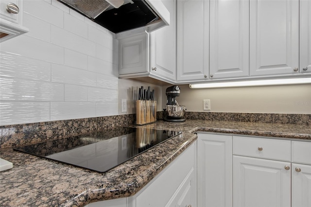 kitchen with dark stone countertops, white cabinetry, black electric stovetop, and range hood