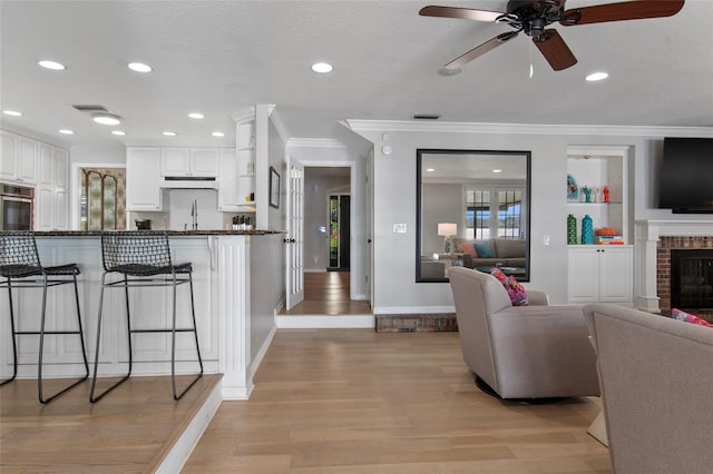 living room featuring a textured ceiling, ceiling fan, light wood-type flooring, and crown molding