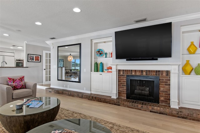 living room featuring hardwood / wood-style flooring, ornamental molding, a textured ceiling, and a brick fireplace