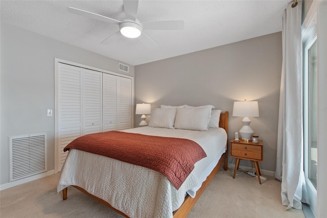 bedroom featuring ceiling fan, a closet, light carpet, and a textured ceiling