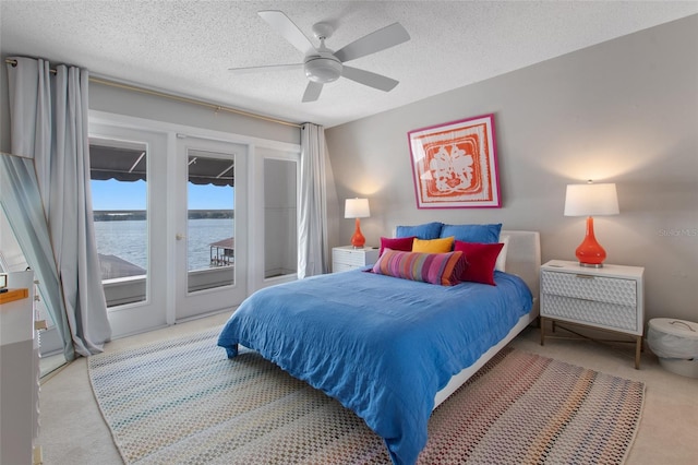 carpeted bedroom featuring access to exterior, a textured ceiling, a water view, and ceiling fan