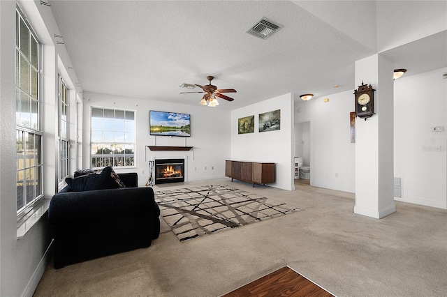 living room with light carpet, ceiling fan, and a textured ceiling