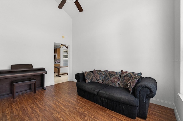 living room featuring dark wood-type flooring, ceiling fan, and a towering ceiling