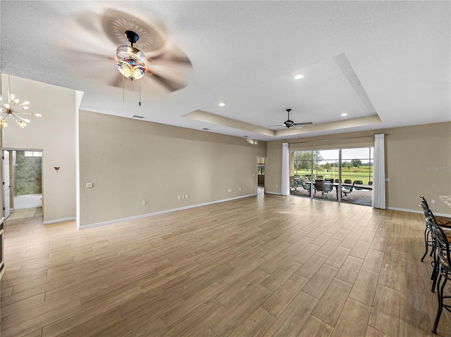 unfurnished living room with light wood-style flooring, a tray ceiling, baseboards, and ceiling fan with notable chandelier