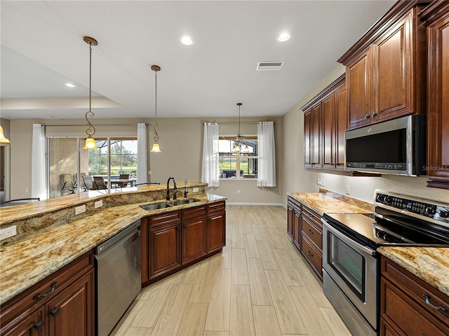 kitchen featuring visible vents, appliances with stainless steel finishes, decorative light fixtures, light stone countertops, and a sink