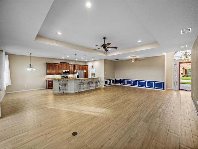 unfurnished living room with a tray ceiling, light wood-type flooring, visible vents, and baseboards