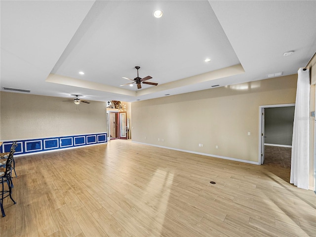 unfurnished living room featuring light wood-style floors, a raised ceiling, visible vents, and baseboards