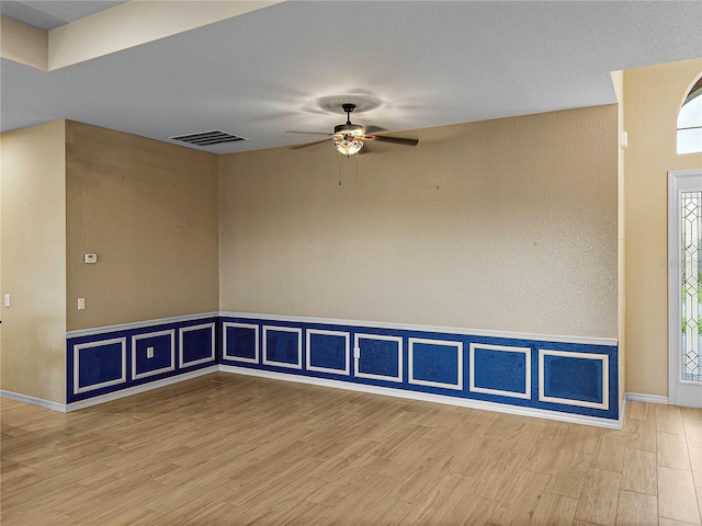 spare room with a ceiling fan, visible vents, baseboards, and wood finished floors