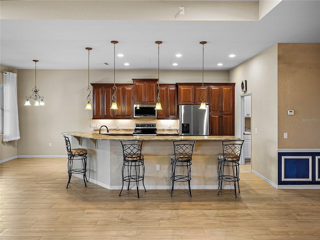 kitchen with an island with sink, a kitchen bar, stainless steel appliances, and decorative light fixtures