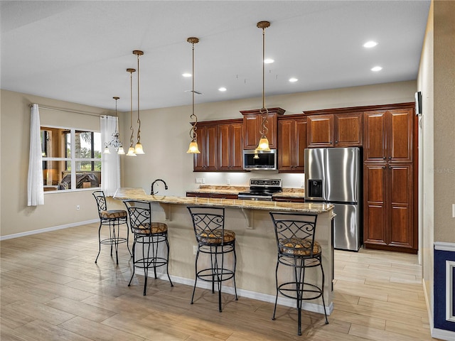 kitchen featuring a breakfast bar area, a kitchen island with sink, stainless steel appliances, light stone countertops, and decorative light fixtures