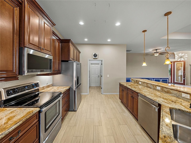 kitchen featuring stainless steel appliances, a sink, light stone countertops, light wood finished floors, and decorative light fixtures