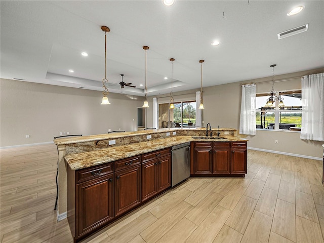 kitchen with a sink, a tray ceiling, pendant lighting, and dishwasher