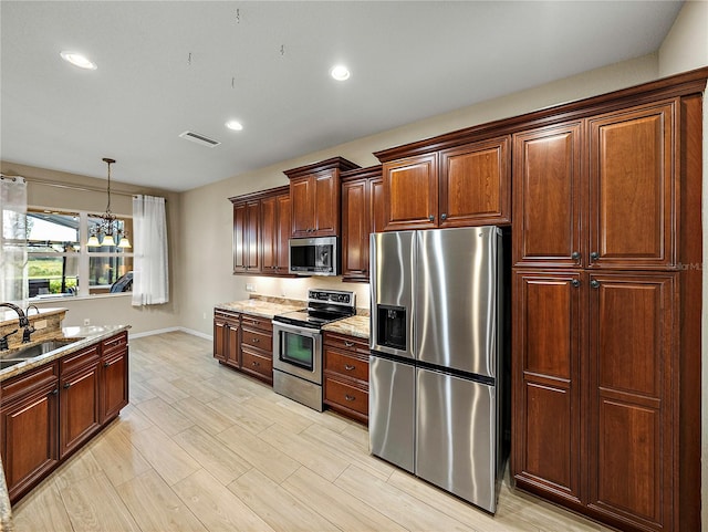 kitchen with pendant lighting, stainless steel appliances, visible vents, a sink, and light stone countertops