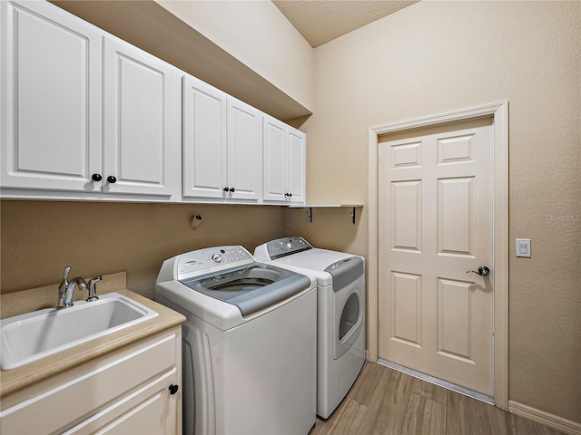 laundry room featuring cabinet space, baseboards, washer and clothes dryer, light wood-type flooring, and a sink