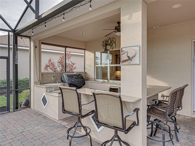 view of patio featuring ceiling fan, a lanai, outdoor wet bar, a sink, and a grill