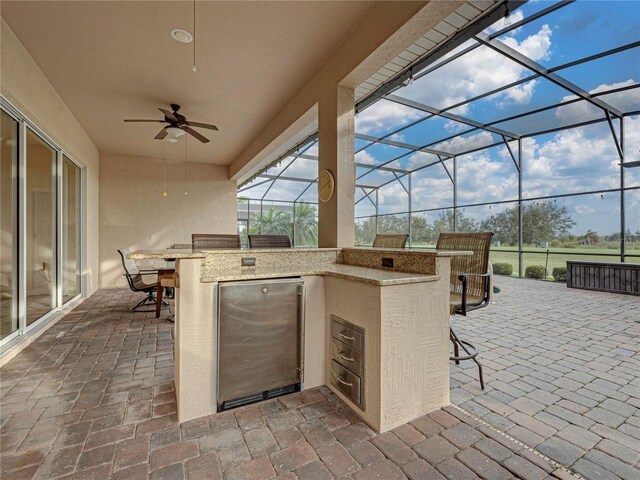 view of patio / terrace with outdoor wet bar, a lanai, ceiling fan, and an outdoor kitchen