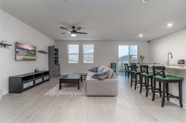 living room with light wood-type flooring, ceiling fan, and a healthy amount of sunlight