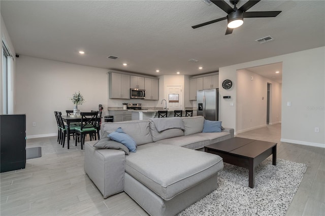 living room with ceiling fan, sink, a textured ceiling, and light hardwood / wood-style flooring