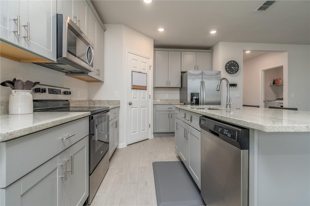 kitchen featuring sink, stainless steel appliances, an island with sink, light hardwood / wood-style floors, and gray cabinets