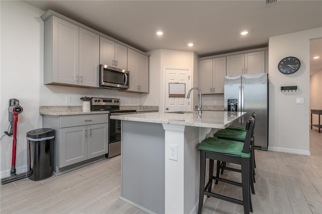 kitchen with gray cabinets, a kitchen island with sink, and appliances with stainless steel finishes