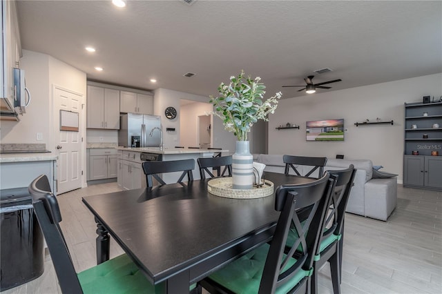 dining room with ceiling fan, sink, light hardwood / wood-style floors, and a textured ceiling