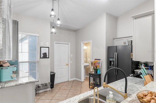 kitchen featuring sink, stainless steel fridge, light tile patterned floors, decorative light fixtures, and light stone counters