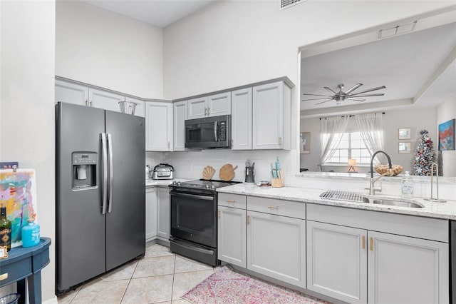 kitchen with gray cabinetry, sink, light stone counters, light tile patterned floors, and appliances with stainless steel finishes