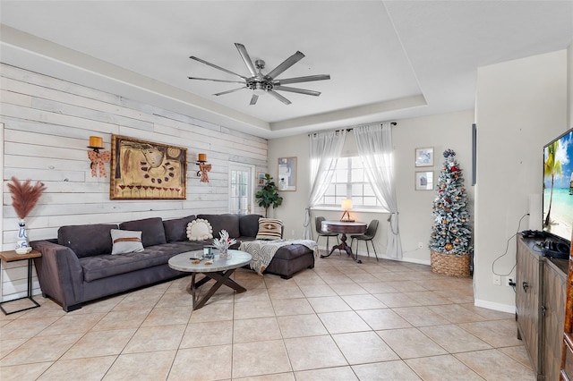 tiled living room with ceiling fan, a raised ceiling, and wooden walls