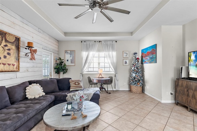 tiled living room featuring a raised ceiling, wooden walls, and ceiling fan