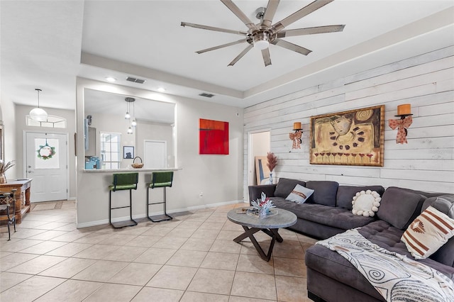 living room featuring light tile patterned flooring, ceiling fan, and wood walls