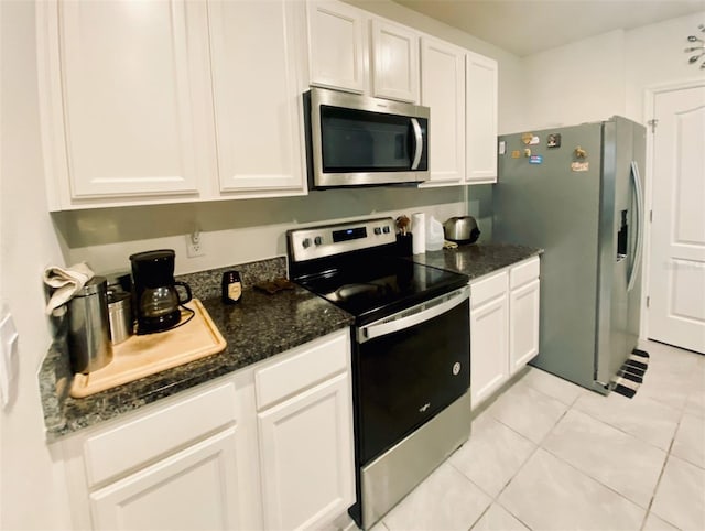 kitchen with dark stone countertops, white cabinetry, light tile patterned floors, and appliances with stainless steel finishes