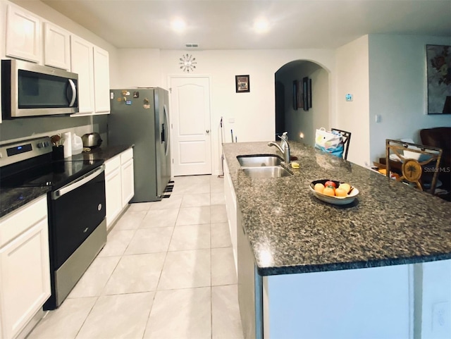 kitchen with appliances with stainless steel finishes, light tile patterned floors, sink, white cabinets, and a kitchen island with sink