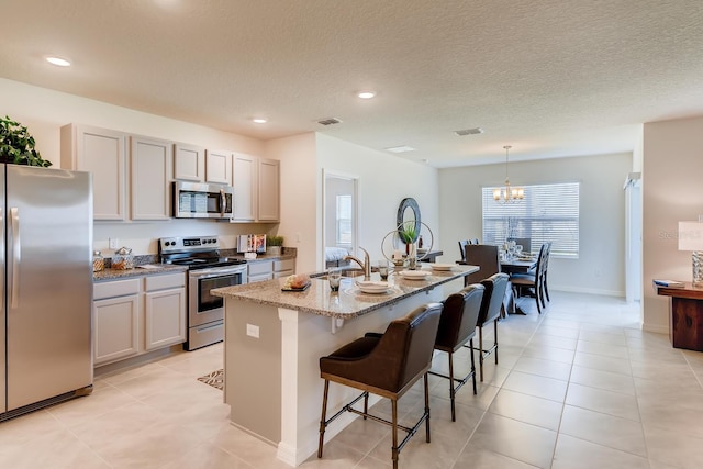 kitchen featuring stainless steel appliances, a center island with sink, light stone counters, a kitchen bar, and hanging light fixtures