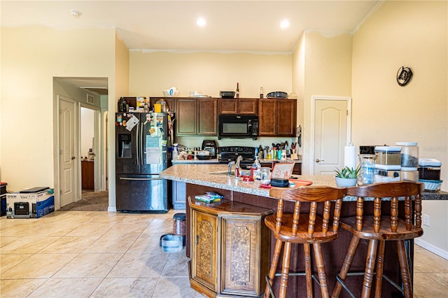 kitchen with light tile patterned floors, a kitchen island with sink, a breakfast bar area, and black appliances