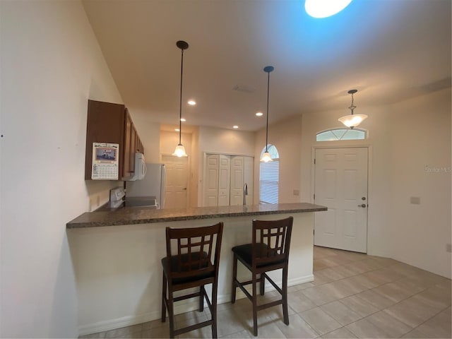 kitchen featuring pendant lighting, white appliances, light tile patterned flooring, a kitchen bar, and kitchen peninsula