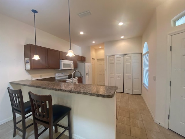 kitchen featuring kitchen peninsula, a kitchen breakfast bar, white appliances, pendant lighting, and light tile patterned floors